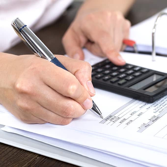 An office worker looks at a calculator, and writes numbers on a printed spreadsheet