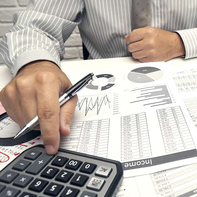 An office worker adds numbers on a calculator, and references a printed spreadsheet with charts